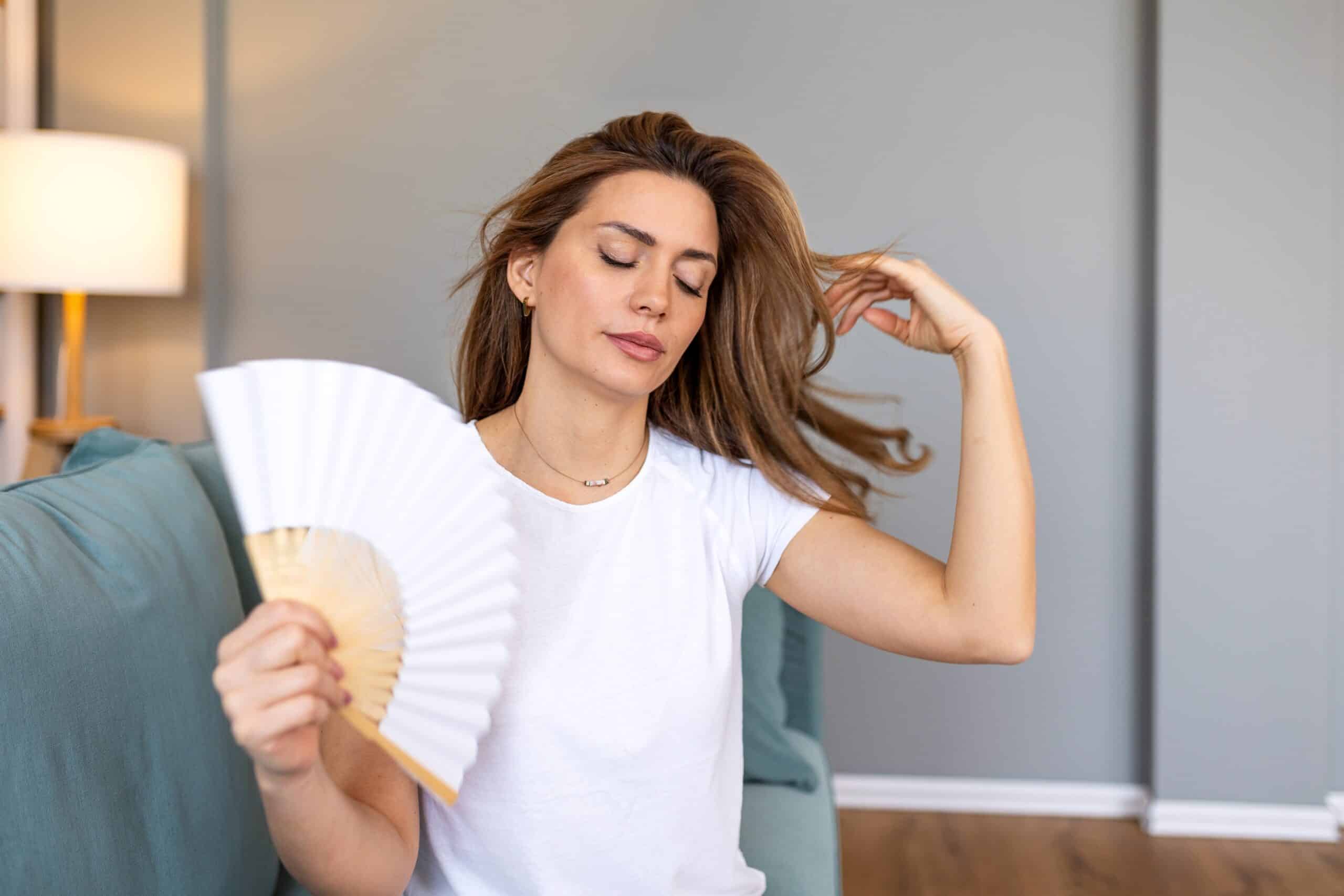 Young,Woman,Sitting,On,Sofa,Using,A,White,Hand,Fan